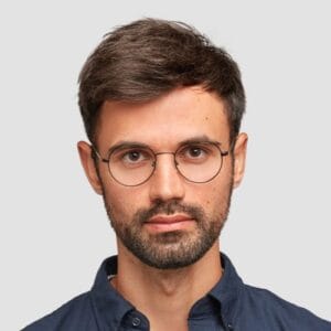 waist-up-portrait-handsome-serious-unshaven-male-keeps-hands-together-dressed-dark-blue-shirt-has-talk-with-interlocutor-stands-against-white-wall-self-confident-man-freelancer
